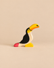 A handcrafted Holztiger Toucan wooden figurine with a yellow beak, black body, and a red-tipped tail.
