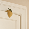 A yellow, lemon-shaped Konges Sloejd Door Stopper - Lemon with a green leaf perched on the top edge of a door.