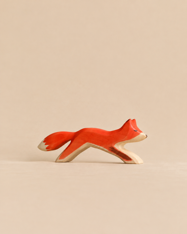 Handmade Holzwald Running Fox, a hand-carved wooden toy of a fox in a running pose, painted in orange and white.