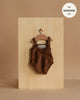 A Minikane 13" Doll Clothing Anna Leotard in Shiny Lycra - Chocolate Brown hangs on a wooden hanger against a light wood board, labeled "fits Minikane Gordis dolls 13 inch." Expertly made in France for your doll collection.