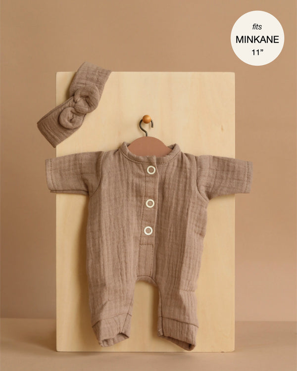 The Minikane 11" Doll Clothing | Lili Jumpsuit & Headband in Cotton Gauze - Mocha is shown on a wooden hanger against a light wood panel, featuring white buttons and a matching knotted headband. Made in France.