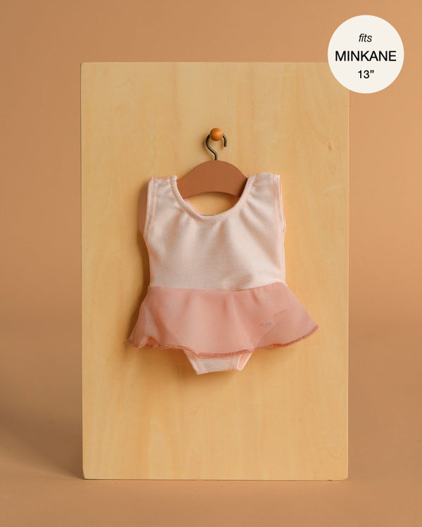 The Minikane 13" Doll Clothing | Ludmila Ruffled Leotard in Nude Pink lycra and chiffon with a sheer skirt hangs on a wooden hanger against a light wood board. Text reads: "fits Minikane Gordis dolls 13”.