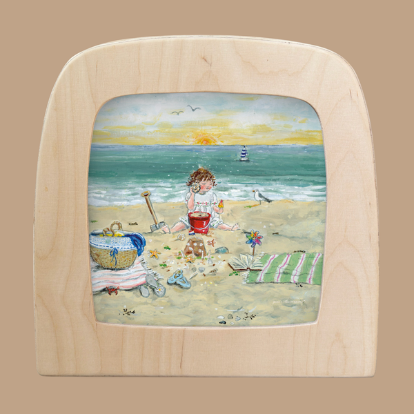 A child plays with a red bucket on a sandy beach, surrounded by seashells, a towel, and a basket. A sailboat and sunset complete the scene—perfect for home decor with the "Silhouette Only - I Hear the Sea for Toverlux Lamp.