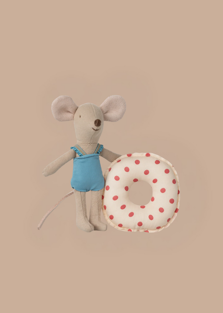 The Maileg Beach Mouse With Float, Little Sister - Red Dot features a little sister mouse in a blue swimsuit standing next to a red polka dot donut float, creating a charming summer scene against a beige background.