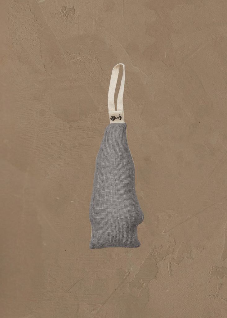 The Coral & Tusk North Pole Bear Ornament hangs against a textured beige wall, its gray fabric and white loop handle adding a cozy, festive touch reminiscent of classic Christmas tree decorations.