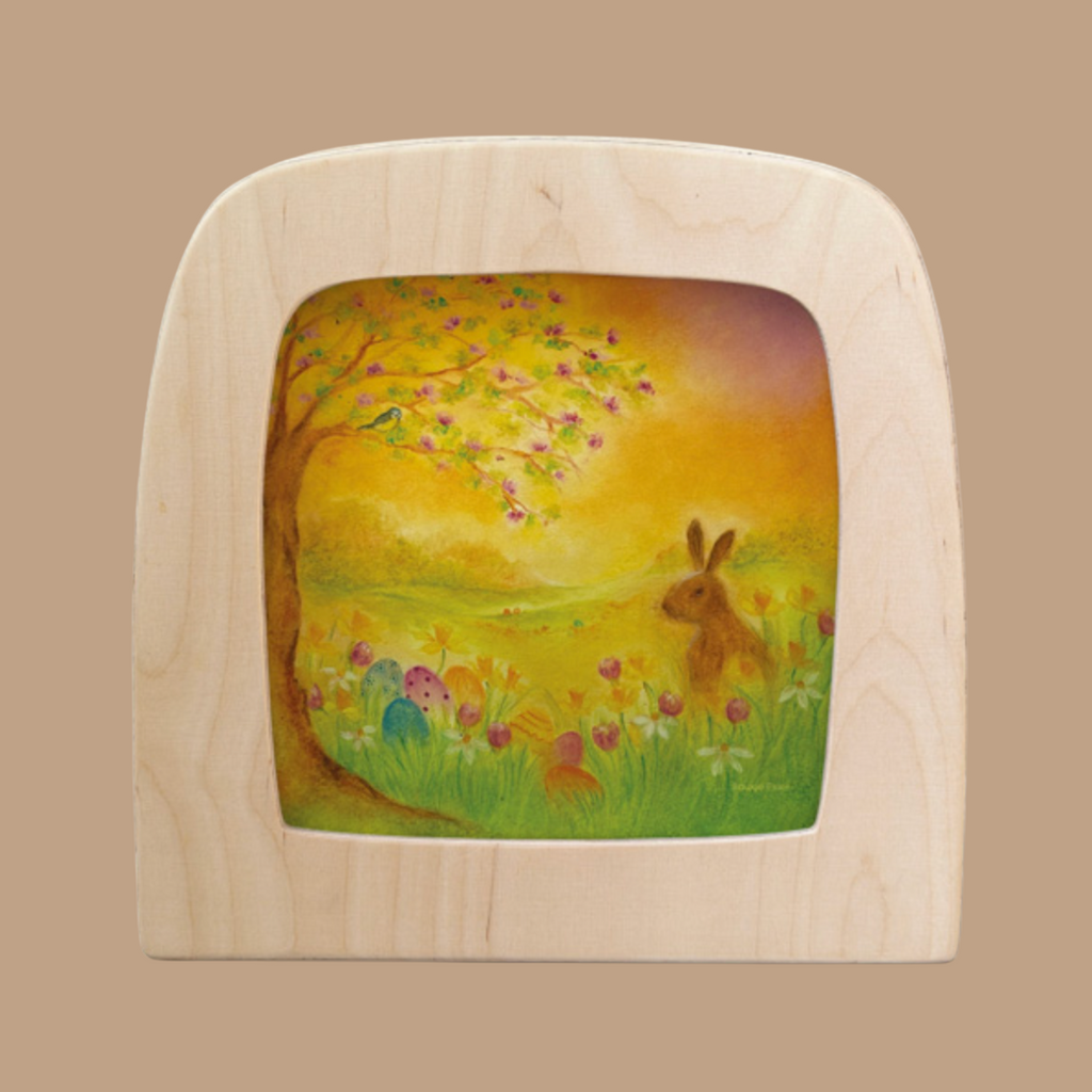 The Silhouette Only - Egg Hunt for Toverlux Lamp features a wooden frame with a vibrant rabbit illustration in a meadow, including a tree with pink blossoms, pastel Easter eggs, and birds perched under a glowing sky—perfect for enhancing your home decor.