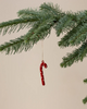 The Maileg Christmas Metal Ornament - Sugar Cane - Dot, a hand-painted red candy cane with white dots, hangs from a thread on a green pine branch against a plain beige background.