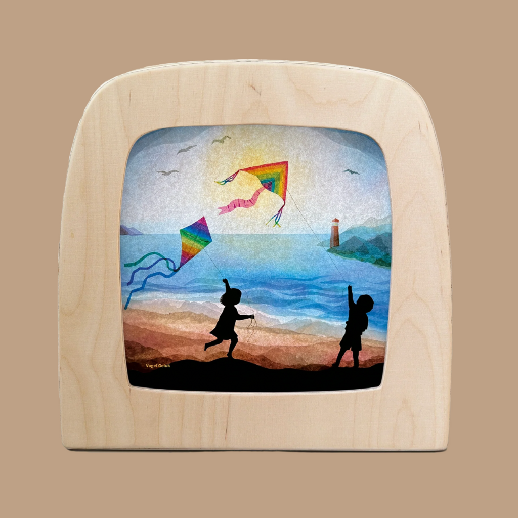 A framed painting titled "Silhouette Only - Kite for Toverlux Lamp" depicts children flying kites on a beach, echoing Magic Silhouettes. A lighthouse, birds, and a blue sky complete the scene, enhanced by an enchanting wooden arch-shaped frame.