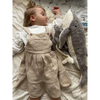 A young child with light hair sleeps on a bed, wearing a beige dress and white top, holding the Senger Naturwelt Cuddly Animal - Whale. She rests on light-patterned organic cotton bedding for extra comfort.