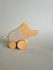 The Pull and Push Toy Little Wild Boar is a handcrafted wooden toy featuring a curving form with light gray paint, white stripes, and rests on a light green background, highlighting the charm of sustainable materials.