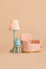 A small pink plush armchair, the Maileg Stool Set, Mouse in mint and light yellow with a vintage paint finish and a matching teapot on top, and a lamp with a patterned shade, all set against a beige background.