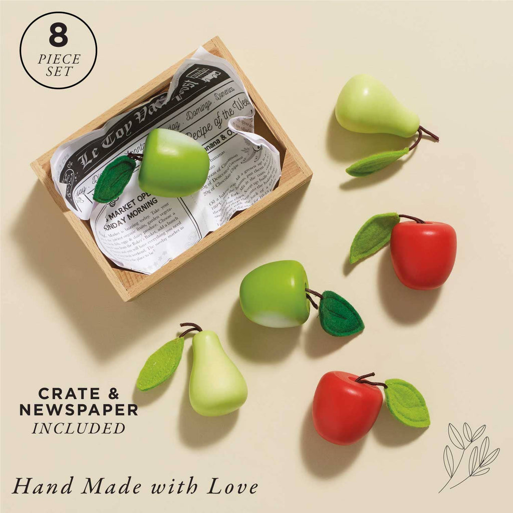 The Orchard Fruits Wooden Market Crate includes eight handmade wooden fruit models—green/red apples and pears, with felt leaves. Perfect as a learning toy, it comes in a wooden crate with vintage-style newspaper. Bottom text: "Crate & Newspaper Included" and "Hand Made with Love.
