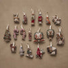 A Coral & Tusk Red Cardinal Ornament among a collection of seventeen assorted embroidered fabric ornaments on natural linen, featuring animals, candy canes, and holiday themes.