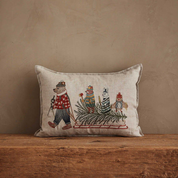 Coral & Tusk Christmas Tree Sled Pillow made of embroidered linen, featuring a bear pulling a sled that carries a Christmas tree, a fox, a llama, and an owl.