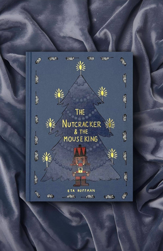 A blue hardcover, "The Nutcracker | Collector's Edition," rests on silky dark fabric. Ballet motifs with a Christmas tree, nutcracker, candles, and mice border the cover of this classic fairy tale.