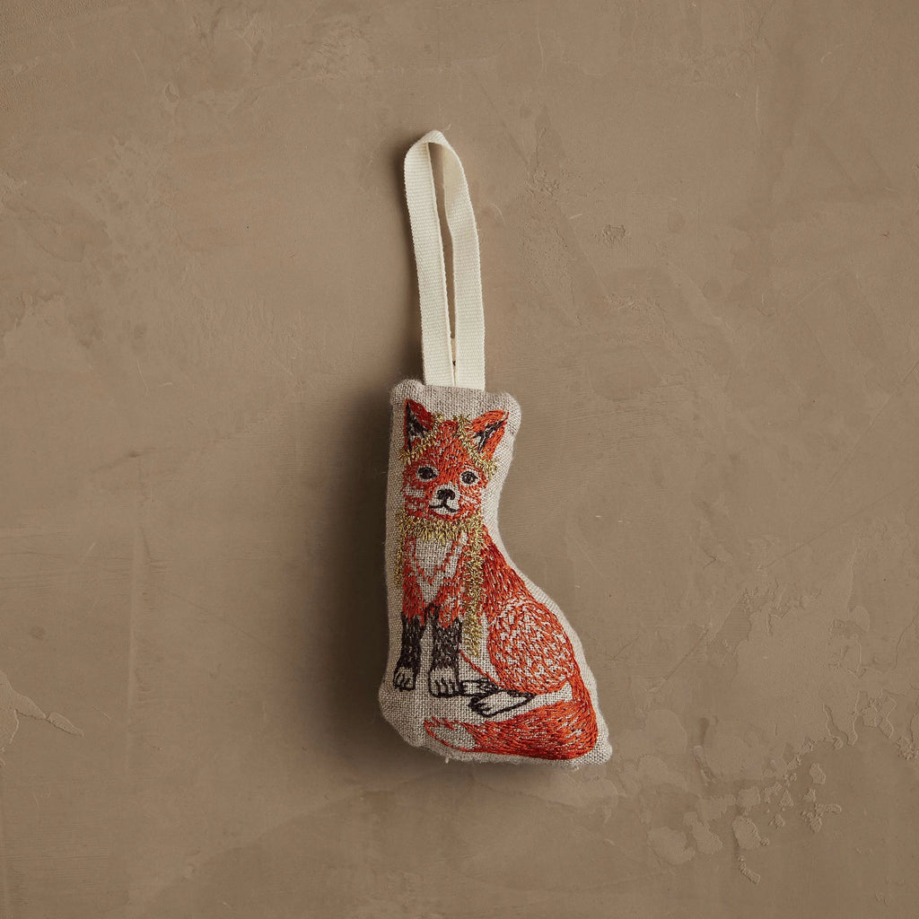 The Coral & Tusk Fox Tree Trimmer Ornament is a small, fabric Christmas ornament shaped like a fox, embroidered in orange, white, and black on beige, with a white ribbon loop—perfect for holiday gifting or decorating your tree.