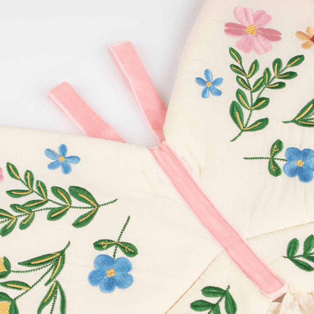 The Meri Meri Butterfly Wings feature a natural cotton pad embroidered with blue, pink, and yellow flowers and green leaves, accented by butterfly wings-inspired pink fabric straps and a pink trim.