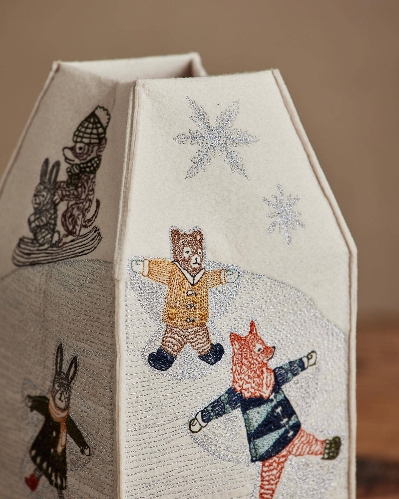 The Coral & Tusk Snow Day Tissue Box Cover features embroidered foxes and a bear ice skating, plus a sledding rabbit and silver snowflakes, making it perfect winter decor.