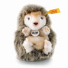 The Steiff Joggi Baby Hedgehog Stuffed Plush Toy, 4 inches, features soft brown and white fur, tiny paws, a black nose, Steiff’s yellow ear tag, and sits upright with the Steiff Original label on its chest.