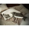 Two Senger Naturwelt Cuddly Animal Dolphin plush toys, one large and one small, sit on cream pillows and a beige textured blanket atop a cozy bed. These soft dolphins are crafted from sustainable materials.