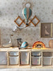 A children's room with wooden storage cubes, colorful bins, the Hot Air Balloon - Pastel Green decoration, a goose statue, a rainbow-shaped light, and framed artwork set against floral wallpaper.