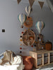A cozy children's room features a mint green and grey Hot Air Balloon wall decor, a circular shelf with toys, wicker baskets, a soft bean bag, a wooden cabinet with storage boxes, and a pennant banner hanging above.
