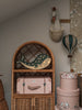 A cozy nursery corner features a rattan shelf with a light-up whale, pink suitcase, and floral hat boxes. Above it hang a fabric horse head in a basket and the Hot Air Balloon - Light Brown / Green children's room decoration.