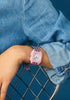 A person in a blue denim shirt rests their arm on a metal chair, showcasing the Mini Kyomo Watch - Lavender Field on their wrist against a blue background.