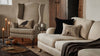Cozy living room with striped armchair, beige sofa, Coral & Tusk Blackbird with Acorn Pillow, Halloween-themed pillows, lit candles, small pumpkins, and a Ouija board on a wooden coffee table. Warm neutral rustic decor.