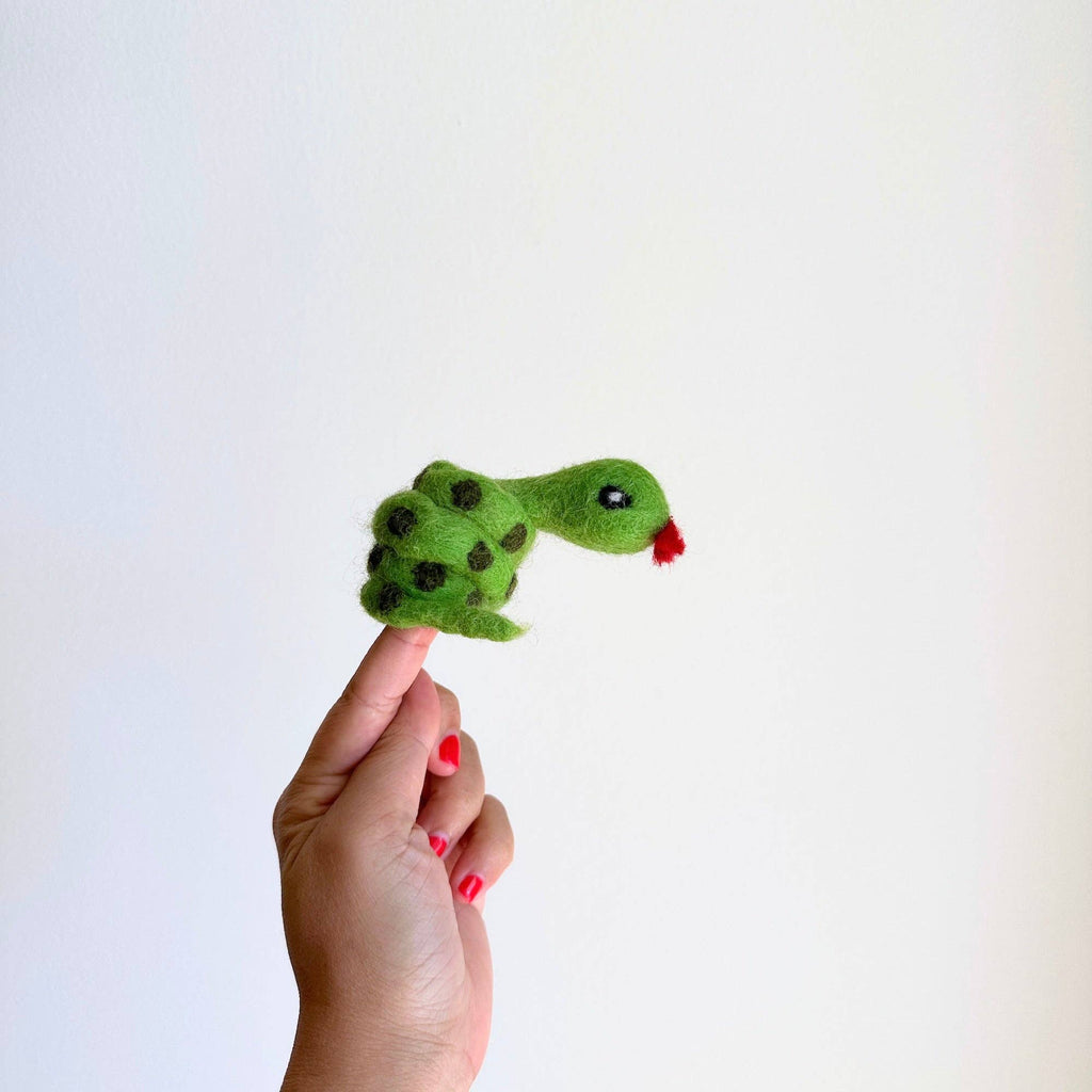 A hand with red-painted nails holds up the Snake Finger Puppet, featuring black spots and a red tongue, perfect for creative storytelling and imaginative play against a plain white background.