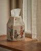 The Coral & Tusk Snow Day Tissue Box Cover, featuring embroidered cats in winter clothes and a snowman, sits on a wooden windowsill beside a sheer curtain. White tissues peek from the top—an adorable accent for snow day decor.
