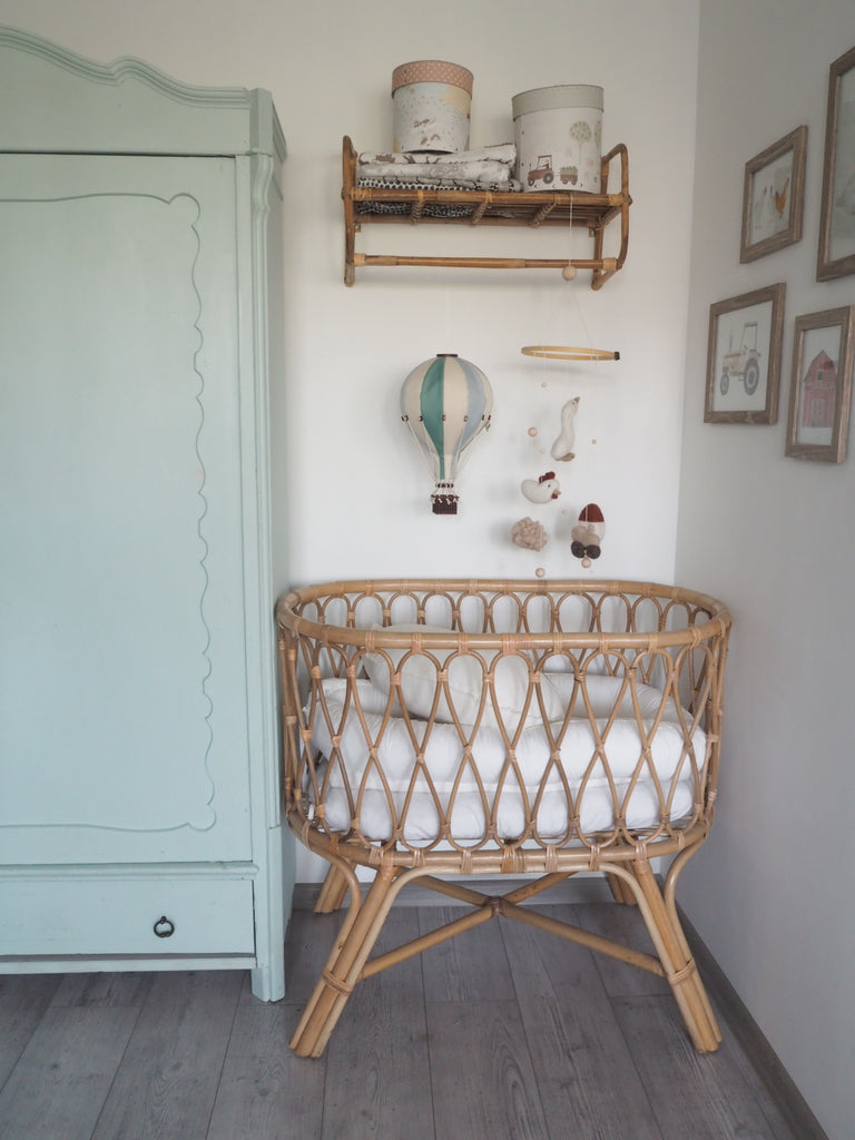 A cozy nursery corner with a rattan crib, wooden shelf, and mint green wardrobe; by the crib hangs the Hot Air Balloon – Mint Green and Grey, its handmade wooden basket adding playful charm to the soft-colored space.
