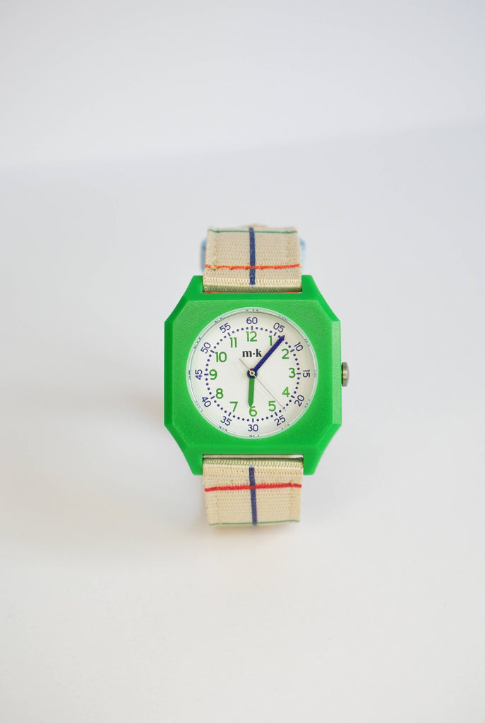 A Mini Kyomo Watch x Taxi Brousse - Color Notebook with a green square case, white dial, black/green numbers, and a beige strap with blue and red stripes is shown against a white background.