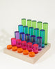 Bauspiel Luminous Pillars 25-Piece Set consisting of twenty-five translucent, colored cylindrical pillars of varying heights arranged in rows on a wooden base.