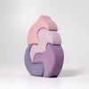 Grimm's Casa Coral Building Blocks features four handpainted wooden puzzle pieces in pastel pink and purple, stacked vertically to form an abstract, curved shape with delicate white line drawings, displayed on a plain white background.