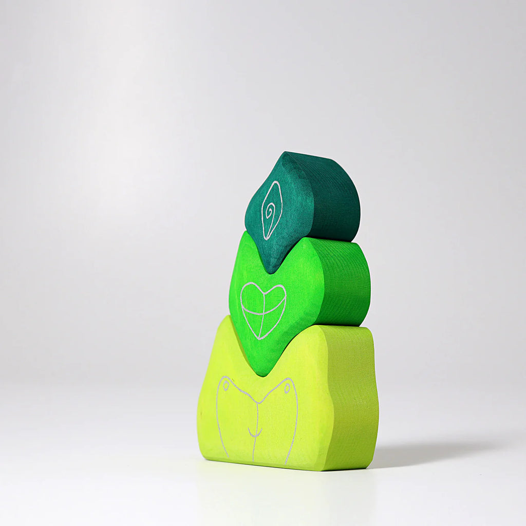 Three green, heart-shaped Grimm's Tower Leaves Building Blocks made from handpainted lime wood are stacked on a white surface. Each block features a simple white line drawing forming an abstract puzzle design.