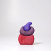 Grimm's Small Bakery Building Blocks feature three organic pieces in red, purple, and violet, stacked in a minimalist bird shape. Smooth surfaces and gold swirl details make them perfect for imaginative wooden play against a white background.