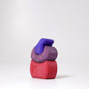 Grimm's Small Bakery Building Blocks—three colorful, curved wooden pieces in red, purple, and blue—are stacked on a white surface against a plain background, sparking imaginative play.