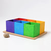 The Grimm’s Small 6 Piece Rainbow Box Sorter features six colorful wooden square boxes arranged in a two-by-three grid on a wooden tray, with a single seashell beside this natural wood toy.
