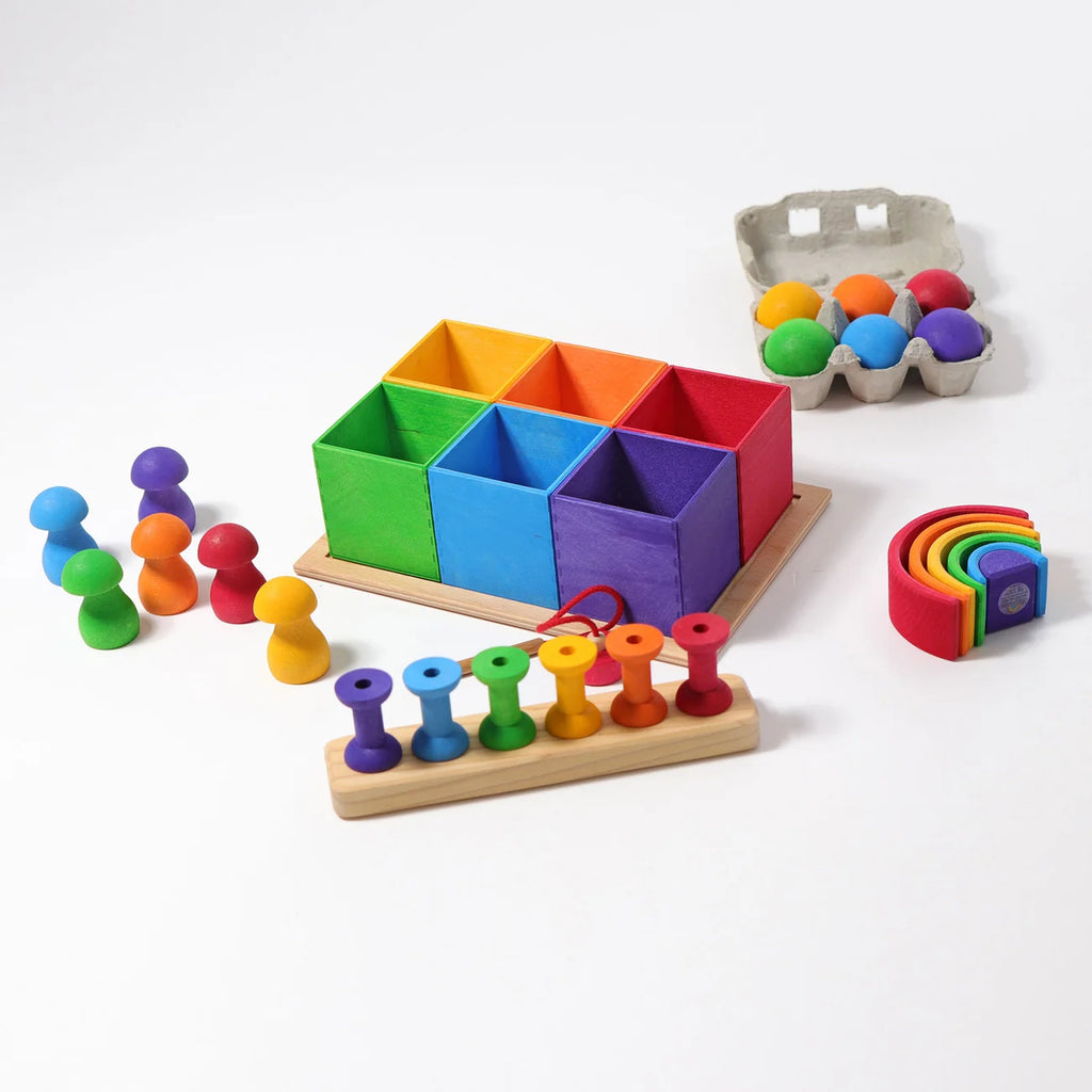 Grimm’s Small 6 Piece Rainbow Box Sorter containing six square boxes, six pegs, six spheres in a natural wood storage box, and a small nested rainbow arch.