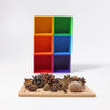 A collection of pinecones, acorns, and a snail shell on a wooden tray in front of six stacked Grimm’s Small 6 Piece Rainbow Box Sorter boxes.