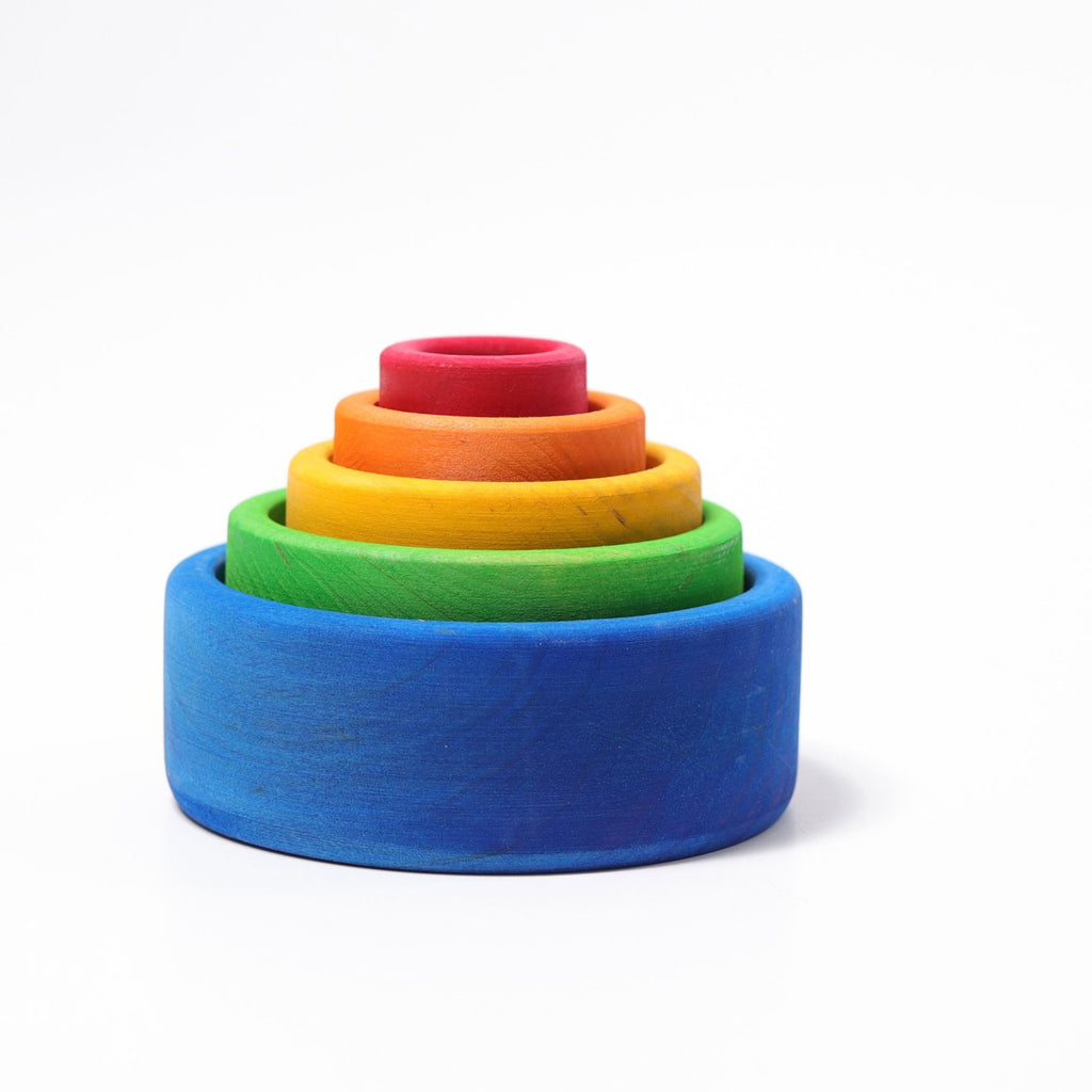 Grimm's Rainbow Stacking Bowls Blue to Red features five colorful wooden bowls, finished with a natural non-toxic stain, arranged by size—blue, green, yellow, orange, and red—on a plain white background.
