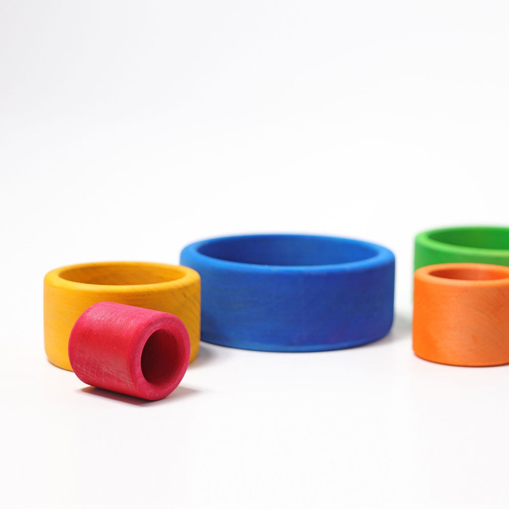 Grimm's Rainbow Stacking Bowls Blue to Red are arranged on a white surface, each in vibrant colors and finished with natural, non-toxic stain for safe play. Some bowls overlap or sit next to each other like a playful stacking display.
