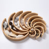 A circular alder-wood sorting tray with concentric, crescent-shaped compartments contains various natural objects like seashells, pinecones, and stones. Made from non-toxic materials, the compartments decrease in size towards the center, creating a visually appealing spiral pattern, similar to Grimm's Large Natural Rainbow Stacker.