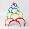 A vibrant and whimsical Grimm's Large Wooden Rainbow displayed in a pyramid arrangement. Each arch, handcrafted from non-toxic wood, features vivid colors: red, orange, yellow, green, blue, purple, and pink. This versatile toy adds a visually appealing touch against a white background.