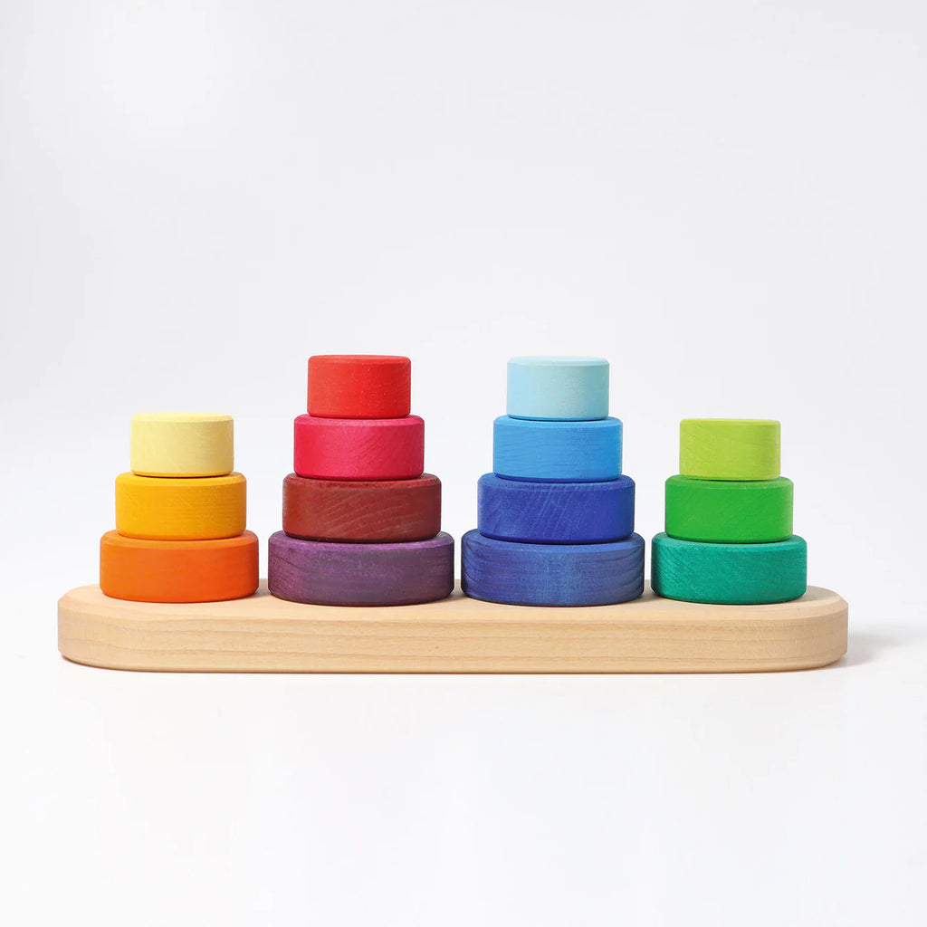 Grimm's Fabuto Stacker features colorful wooden stacking rings in rainbow order on a light wooden base, with five stacks of perfectly coordinated circular pieces, all set against a plain white background.