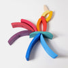 Grimm's Stacking Tower Sailboat's curved, colorful wooden pieces are arranged on a white surface to resemble a parrot, with the vibrant blocks forming its wings, tail, and beak—perfect for building fine motor skills.
