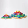 Two square wooden pyramids are arranged on a white background. The smaller is the Grimm's Stepped Pyramid Block Set - Small, while the larger has more layers and brighter colors, resembling the classic Grimms stepped pyramid.