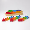Grimm’s Sorting Game Rainbow Bowls with Tweezers featuring six colorful wooden bowls in a tray behind an assortment of rainbow-colored wooden hearts, stars, and fish used for a color sorting game.