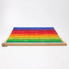 A wooden tray of Grimm’s Stepped Counting Blocks - Large, featuring rows of rainbow-colored wooden building blocks arranged by height with a single snail shell in the foreground.